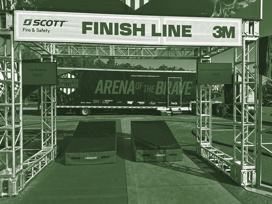 The Firefighter Challenge finish line, with a live result display on each side showing team names and times.